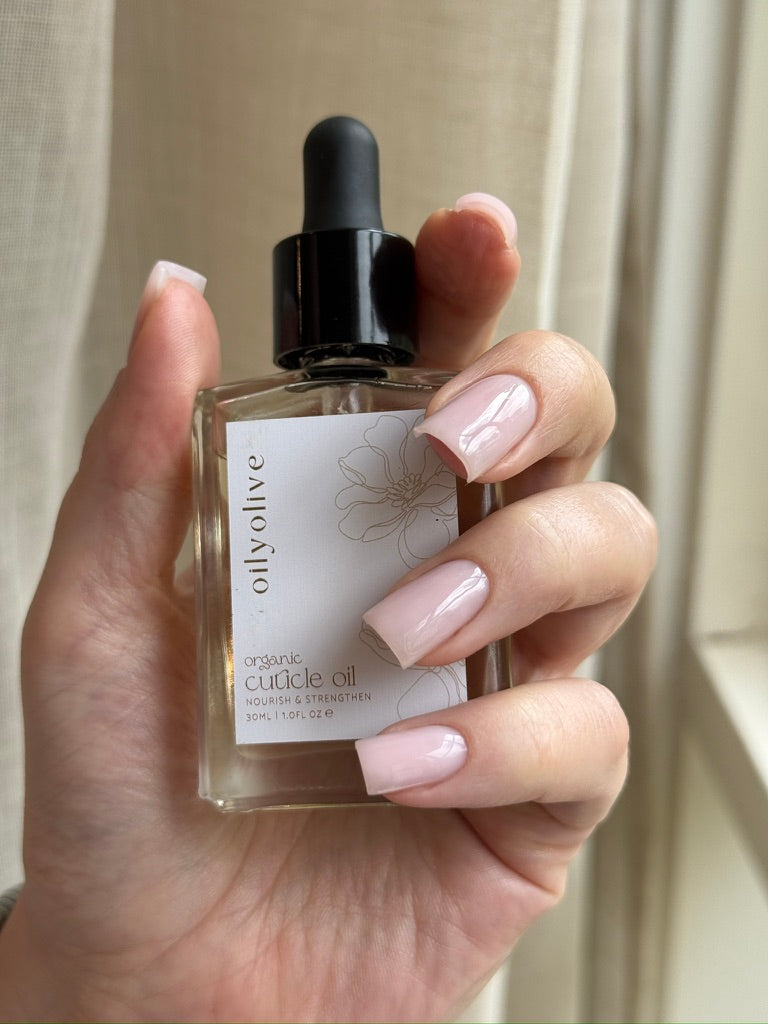 Hand holding a bottle of oily olive organic nail and cuticle oil with a dropper 30ml